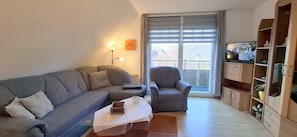 Ein Wohnzimmer mit einer Couch, einem Sessel, einem Couchtisch und einem Fernseher.