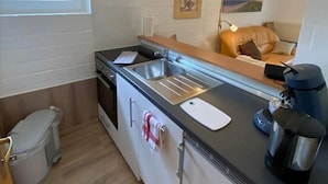 Ett kompakt kök med en diskho, en spis och ett fönster med utsikt över en byggnad.