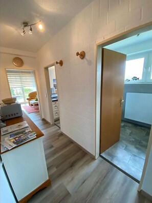 Ein Flur mit Holzboden, weißer Wand mit Ziegeloptik, einer Tür mit runder Klinke und einer Deckenleuchte.