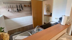 A compact kitchen with a wooden countertop, a hanging utensil rack, a sink, and a visible door leading to another room. - Appartmenthaus Nolting Apartment 2 Nolting with terrace & WLAN in Werdum - (Werdum)