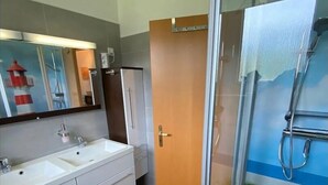 A bathroom with a glass shower enclosure, a double sink vanity, and a door leading to another room. - Appartmenthaus Nolting Apartment 2 Nolting with terrace & WLAN in Werdum - (Werdum)