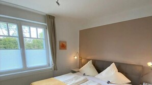 A bedroom with a bed, bedside tables, a window, and a wall-mounted light fixture. - Appartmenthaus Nolting Apartment 2 Nolting with terrace & WLAN in Werdum - (Werdum)
