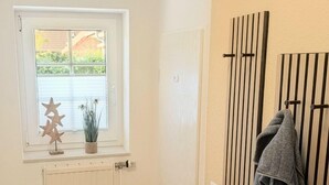 A room with a radiator, a window with a view of greenery, a door with a towel rack, and a wooden floor. - Vacation home Am Kurzentrum 26 No. 3 (Wittmund)