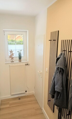 Ein Zimmer mit Heizkörper, einem Fenster mit Blick auf Grünflächen, einer Tür mit Handtuchhalter und einem Holzboden.