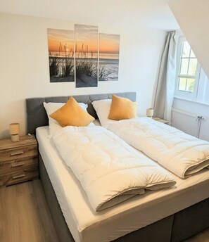 Ein Doppelbett mit weißer Bettwäsche und zwei Kissen, ein Nachttisch mit Lampe und ein Fenster mit Vorhängen.