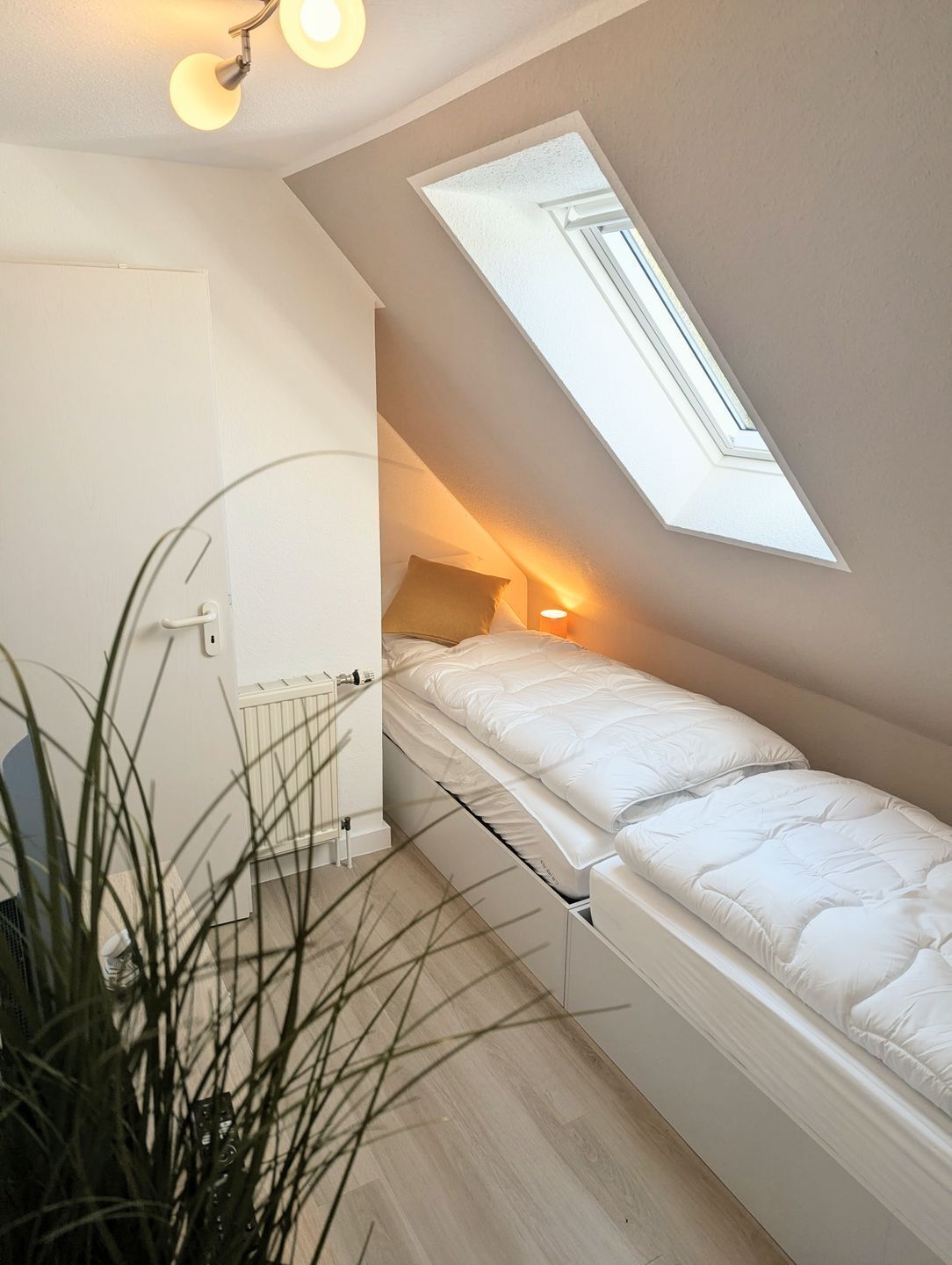 Ein kleines, kompaktes Schlafzimmer mit Dachfenster, einem Bett, einem Nachttisch und einer Heizung.