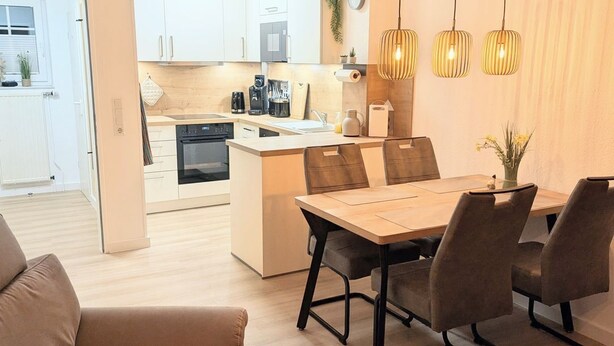 A modern kitchen with white cabinets, a central island, and hanging pendant lights. - Vacation home Am Kurzentrum 26 No. 3 (Wittmund)