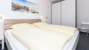 A hotel room with a bed, a desk, a wardrobe, and a painting on the wall. - Deich in Sicht - Holiday apartment "Deich in Sicht" (Neuharlingersiel)