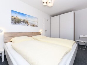 A hotel room with a bed, a desk, a wardrobe, and a painting on the wall. - Deich in Sicht - Holiday apartment "Deich in Sicht" (Neuharlingersiel)