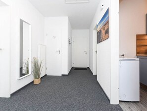 A hallway with white walls, a grey carpet, a potted plant, a door, and a small white appliance. - Deich in Sicht - Holiday apartment "Deich in Sicht" (Neuharlingersiel)