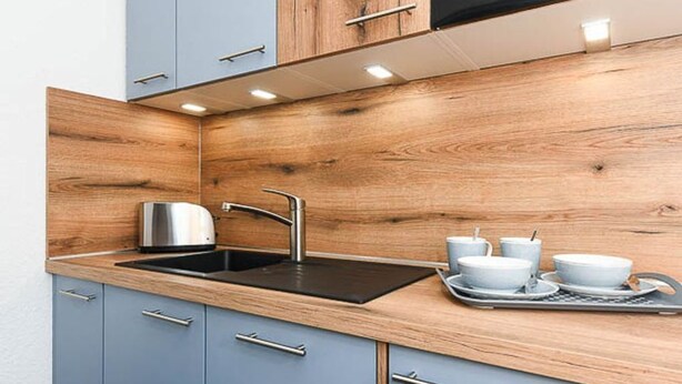 A modern kitchen with a wooden backsplash, a stainless steel sink, and a tray with white dishes. - Deich in Sicht - Holiday apartment "Deich in Sicht" (Neuharlingersiel)