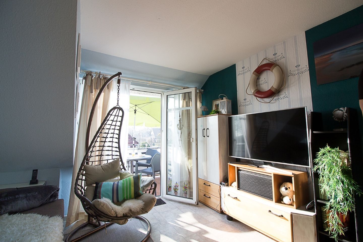 A living room with a TV, a hanging chair, a sliding glass door to a patio, and a bookshelf.
