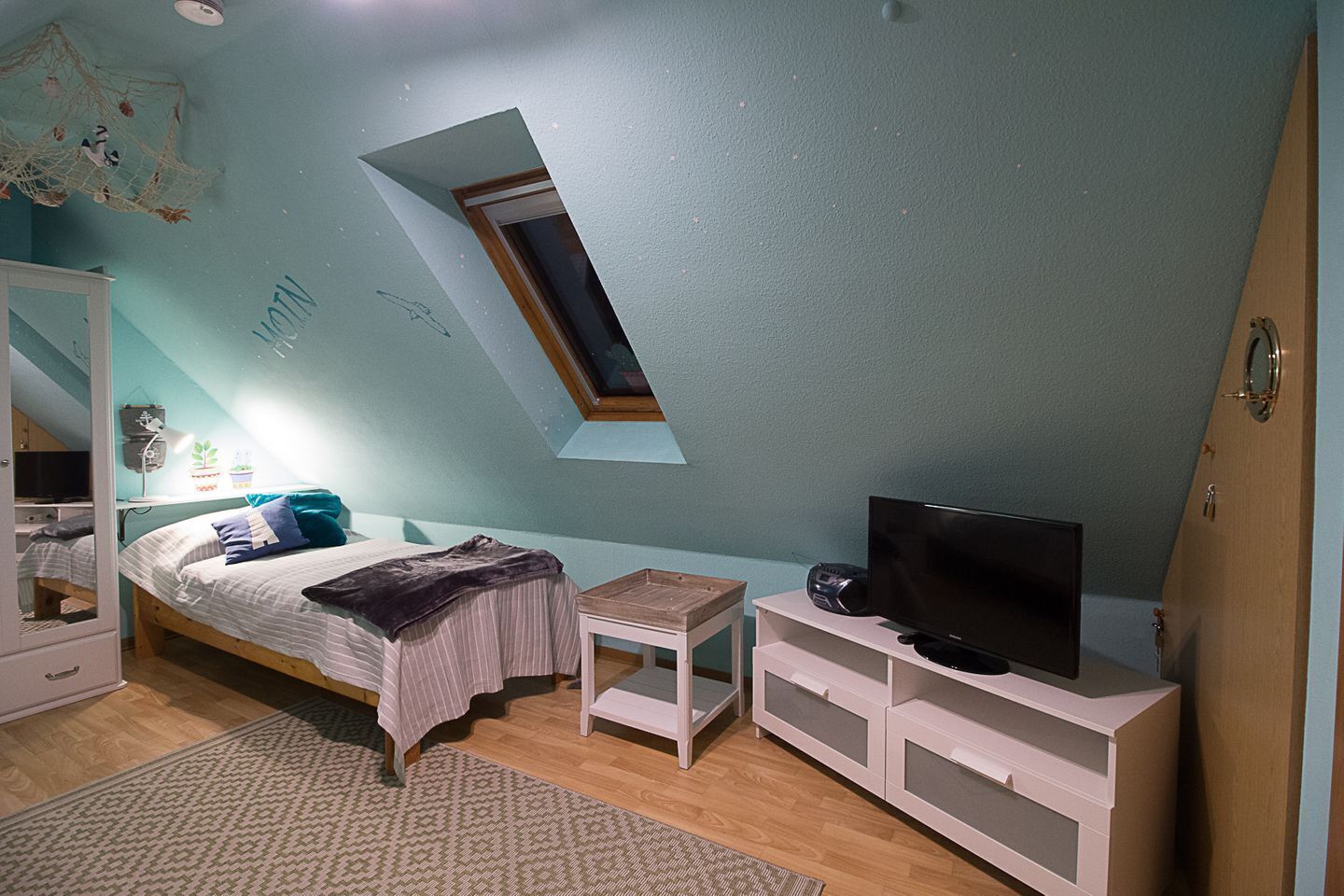 Una camera da letto con soffitto spiovente, un lucernario, un letto, una TV e un armadio.