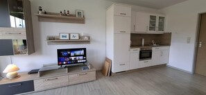 Eine moderne Küche mit weißen Schränken, einem eingebauten Backofen und einem Fernseher auf einer Holztruhe.