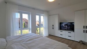 Une chambre à coucher avec un lit, une télévision, des armoires blanches et de grandes fenêtres.