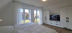 A bedroom with a bed, a TV, white cabinets, and large windows. - End terraced house Alte Schmiederstraße 4g - End terraced house Alte Schmiedestr. 4g (Werdum)