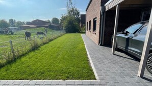 Une allée pavée mène à un bâtiment en briques doté d’un garage, une pelouse entourée d’une clôture et un ciel dégagé.