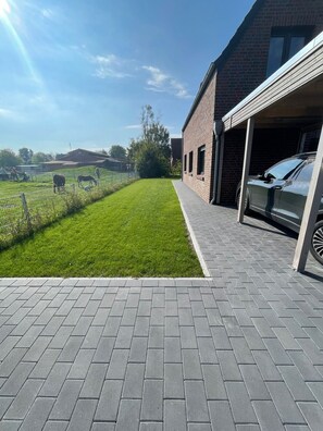A paved driveway leading to a brick building with a garage, a grassy area with a fence, and a clear sky. - End terraced house Alte Schmiederstraße 4g - End terraced house Alte Schmiedestr. 4g (Werdum)