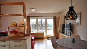 A modern room with a dining table, chairs, a TV, and a large window. - Wohnpark Legewarfen 2/3 - Holiday apartment Wohnpark Legewarfen 2/2 (Werdum)