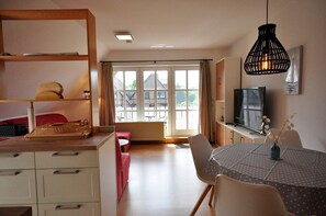 A modern room with a dining table, chairs, a TV, and a large window. - Wohnpark Legewarfen 2/3 - Holiday apartment Wohnpark Legewarfen 2/2 (Werdum)