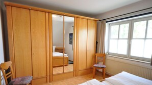 A bedroom with a wooden wardrobe, a single bed, a chair, and a window with curtains. - Wohnpark Legewarfen 2/3 - Holiday apartment Wohnpark Legewarfen 2/2 (Werdum)