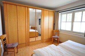 A bedroom with a wooden wardrobe, a single bed, a chair, and a window with curtains. - Wohnpark Legewarfen 2/3 - Holiday apartment Wohnpark Legewarfen 2/2 (Werdum)