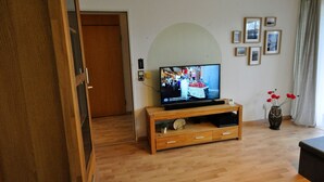 Un salon avec un meuble de rangement en bois pour l’équipement audiovisuel, un téléviseur, un vase rempli de fleurs rouges et des tableaux encadrés accrochés au mur.