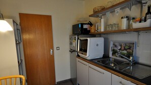 Une cuisine compacte équipée d’un four à micro-ondes, d’un grille-pain et d’un évier. On y trouve une porte en bois, une chaise et une petite table.