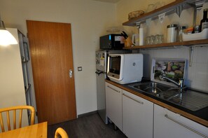 Eine kleine Küche mit Mikrowelle, Toaster und Spüle. Eine Holztür, ein Stuhl und ein kleiner Tisch sind ebenfalls vorhanden.