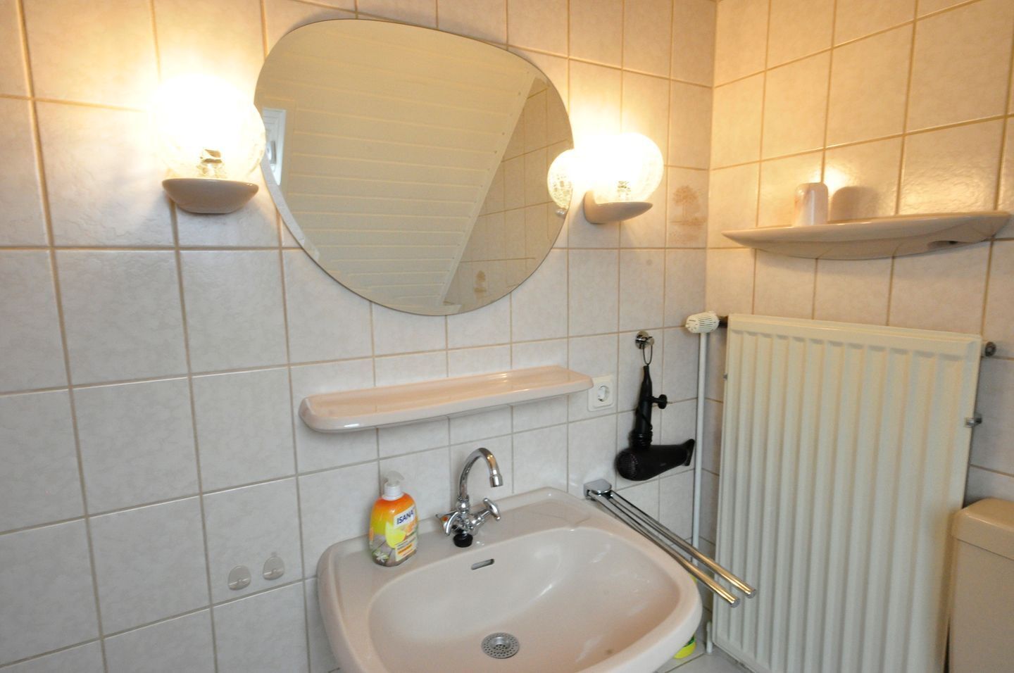 Une salle de bain équipée d’un lavabo, d’un miroir, d’un luminaire et d’un radiateur.