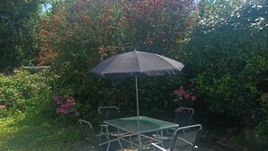Een buitentafel met stoelen en een zwarte parasol, omgeven door groen en struiken.