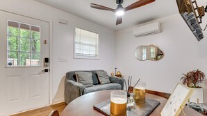 A room with a wooden dining table, a ceiling fan, a window with blinds, a gray sofa, and a wall-mounted air conditioner. - Couple’s Retreat! 7 Mi to Dtwn Atlanta & Six Flags (Atlanta)