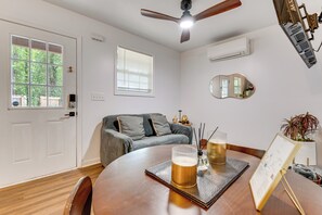 A room with a wooden dining table, a ceiling fan, a window with blinds, a gray sofa, and a wall-mounted air conditioner. - ATL Couple’s Retreat 7 Mi to Mercedes-Benz Stadium (Atlanta)