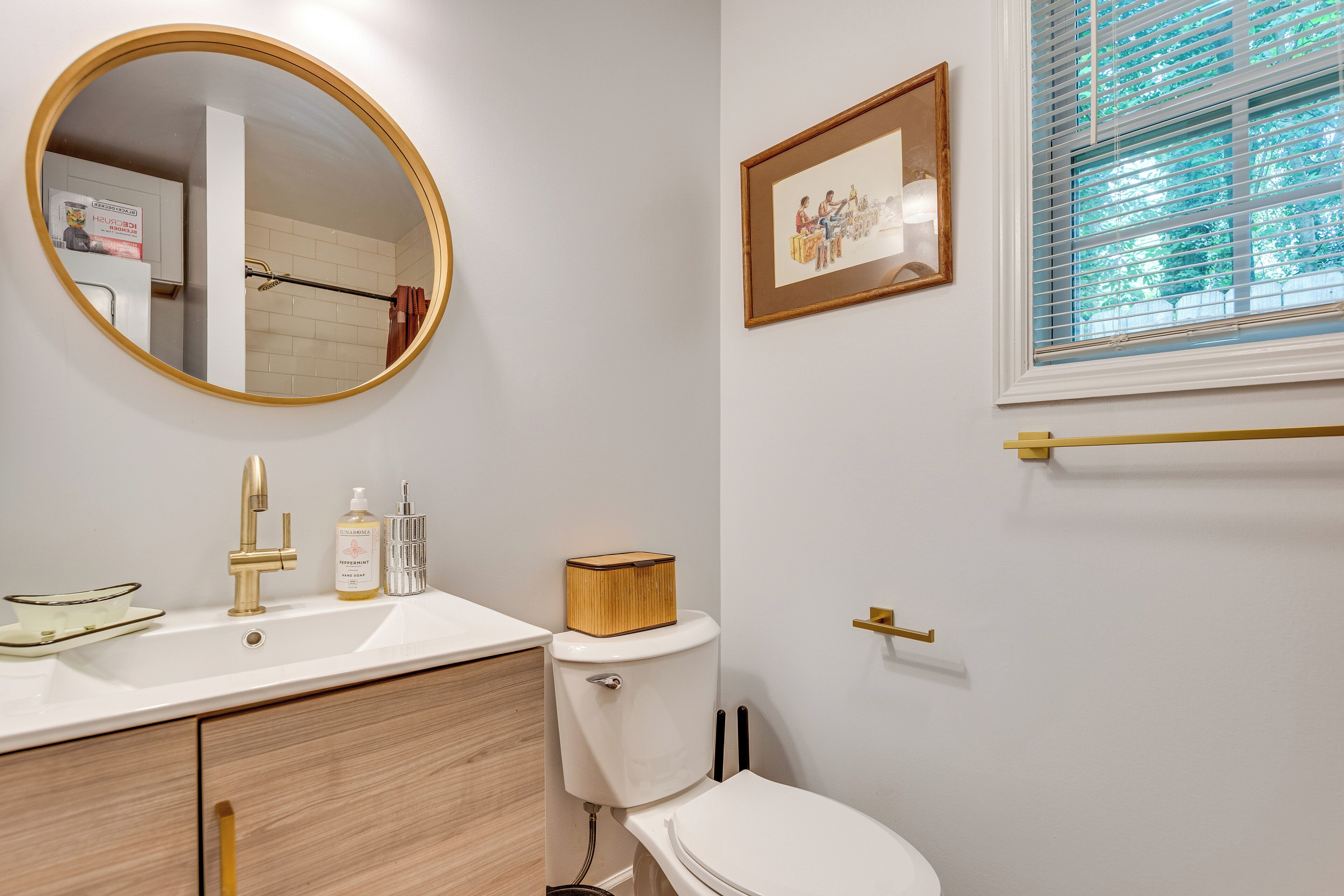 A bathroom with a round mirror, a sink, a toilet, and a framed picture on the wall.