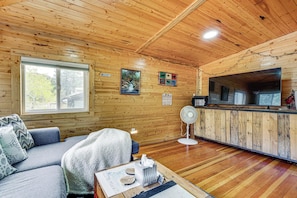 Ein Holzblockhaus-Interieur mit einer Couch, einem Tisch mit Taschentuchbox, einem Ventilator und einem großen Fernseher.