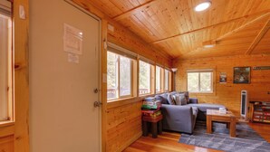 L’intérieur chaleureux d’un chalet, avec un décor en bois, un canapé, une table avec des jeux de société et une fenêtre donnant sur la forêt.