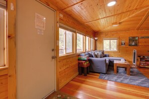 A cozy cabin interior with a wooden interior, a sofa, a table with board games, and a window with a view of trees. - Fish & Hike! Hot Tub Haven 2 Mi to Estes Park (Drake)