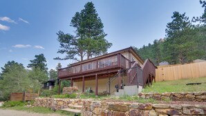 Une cabane à deux étages, avec des fondations en pierre, une terrasse en bois et un escalier menant à l’étage supérieur.