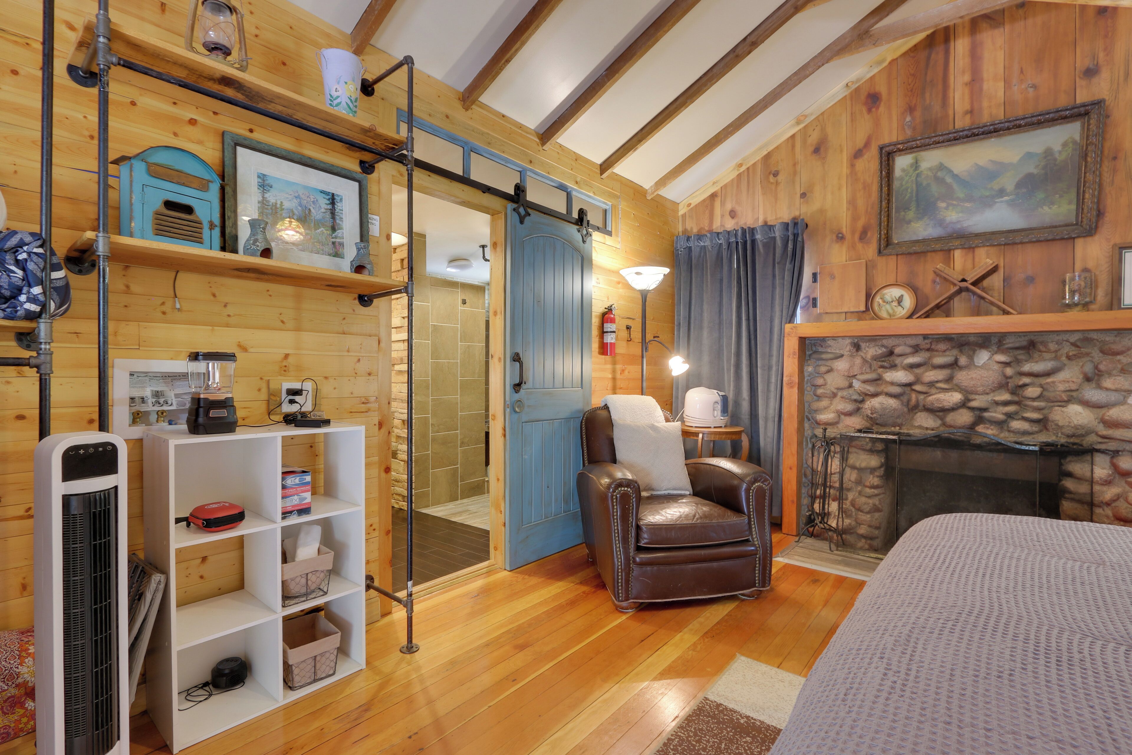 Un interior de cabaña acogedor con chimenea de piedra, un sillón de cuero y piso de madera.