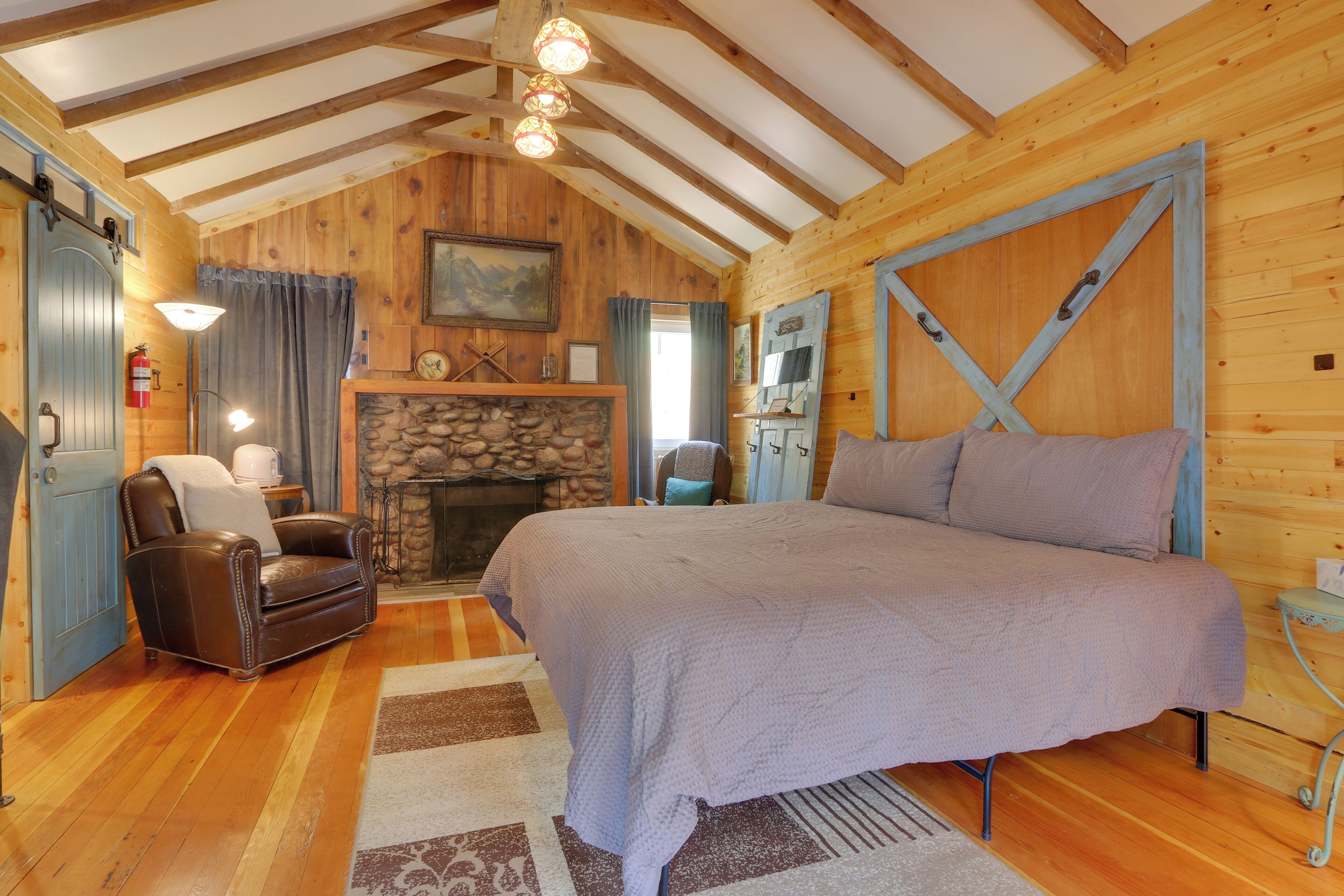 A cozy log cabin bedroom with a large bed, a fireplace, a leather chair, and wooden walls.