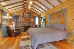 A cozy log cabin bedroom with a large bed, a fireplace, a leather chair, and wooden walls. - Fish & Hike! Hot Tub Haven 2 Mi to Estes Park (Drake)
