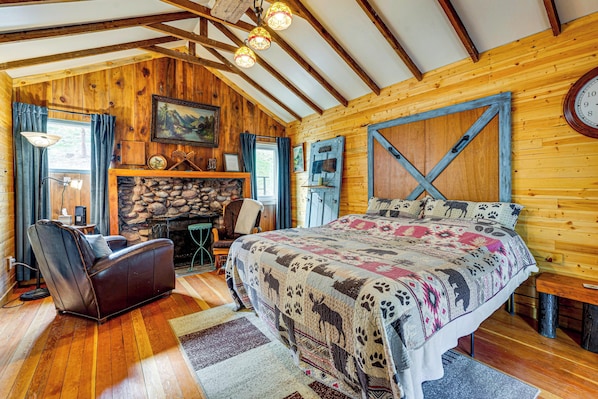 Ein rustikal eingerichtetes Blockhauszimmer mit Kamin, einem Bett mit gemustertem Quilten, einer Ledersofa und Holzbalken an der Decke.