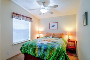 A bedroom with a ceiling fan, a bed with a green and blue patterned bedspread, two bedside lamps, a window with blinds, and a framed picture on the wall. - 'Fox Cabin' - 6 Blocks to Yellowstone Nat'l Park! (West Yellowstone)