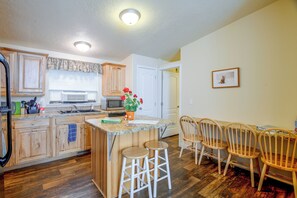 Una cocina con armarios de madera, un microondas y un comedor con sillas y taburetes de madera.