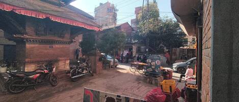 Una escena callejera con edificios, una motocicleta, una bicicleta y un carrito de vendedor con frutas.