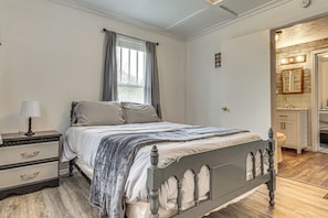 Un dormitorio con cama, mesita de noche y cómoda, un baño con lavabo y espejo, y una ventana con cortinas.