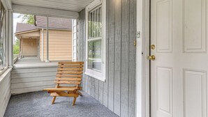 En veranda med en træbænk, en hvid dør og et vindue med udsigt til et hus.