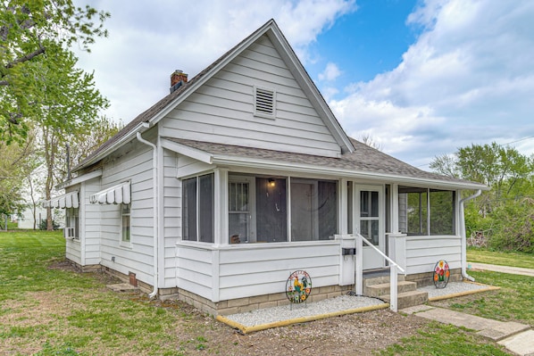 A white two-story house with a covered porch, a chimney, and a small garden area.