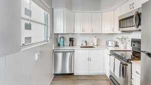 Una cocina moderna con armarios blancos, electrodomésticos de acero inoxidable y un ventanal que proporciona luz natural.