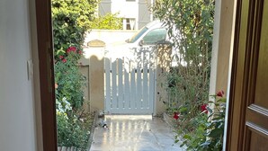A doorway leading to a tiled patio with a white fence, potted plants, and a red mat.